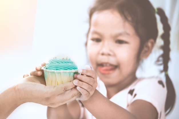 Mother give delicious blue cupcake to child girl and holding together in vintage color tone