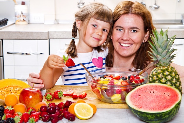 Mother gives to the little girl a fruit salad in the kitchen.