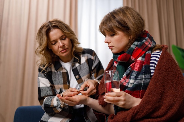 Mother giving pill to her daughter with flu. Woman taking care of a sick girl