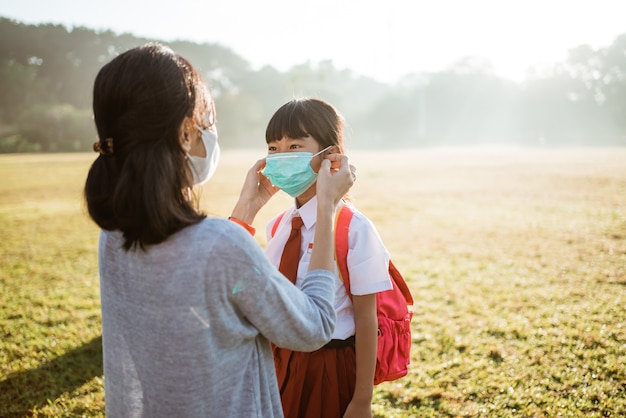 Mother help her daughter to put on the mask before going to school