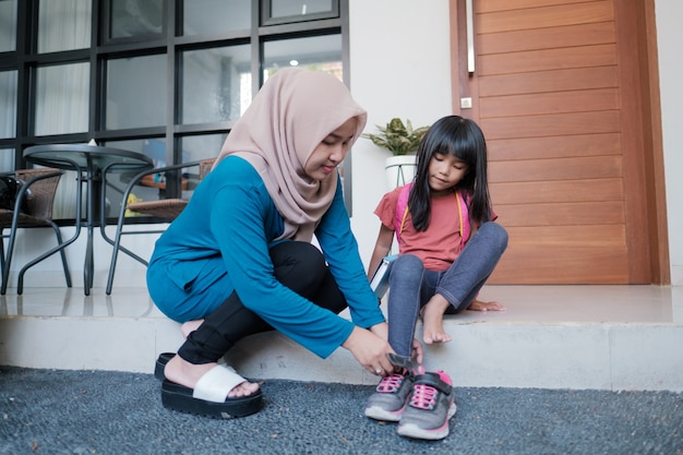 Mother help her daughter to wear a shoes in the morning while preparing to go to school