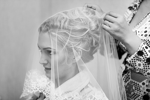 Mother helping young beautiful bride to get dressed for the wedding ceremony. Black and white photography