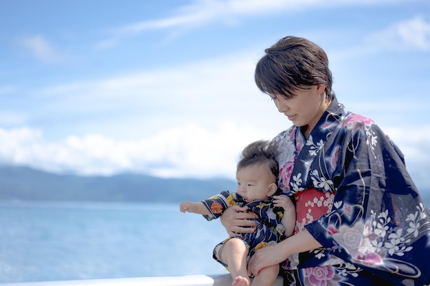 A mother and her baby are standing on a pier by the water.