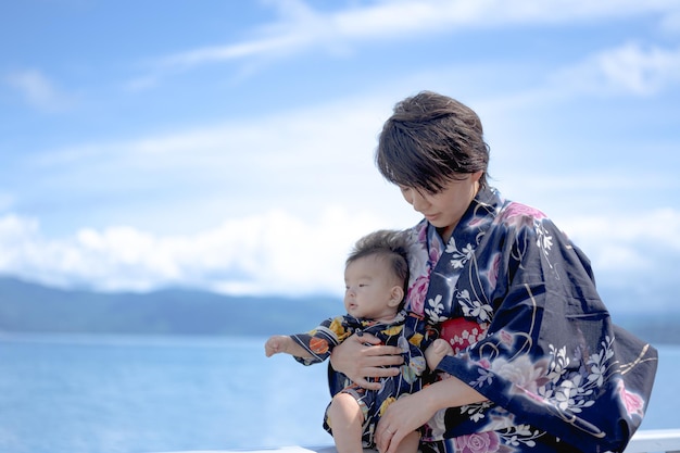 A mother and her baby are standing on a rock by the water.