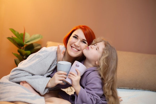 Mother and her baby daughter girl on bed in bedroom.