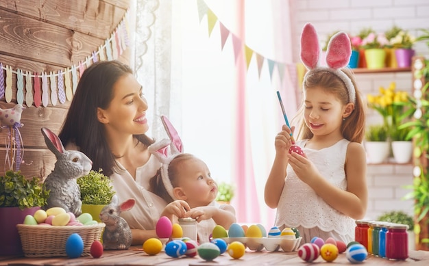 A mother and her daughter are painting eggs. Happy family are preparing for Easter. Cute little child girl wearing bunny ears.