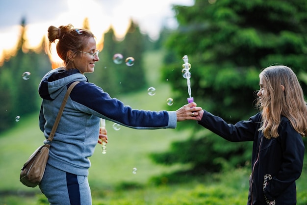 Mother and her daughter blow soap bubbles in the spruce forest during a walk