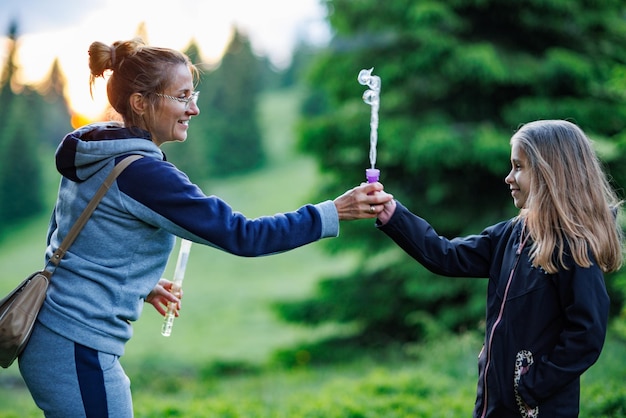 Mother and her daughter blow soap bubbles in the spruce forest during a walk