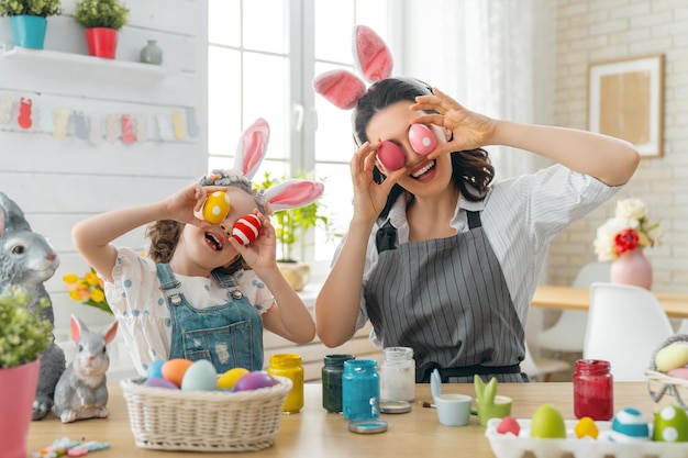 Mother and her daughter painting eggs Happy family preparing for Easter