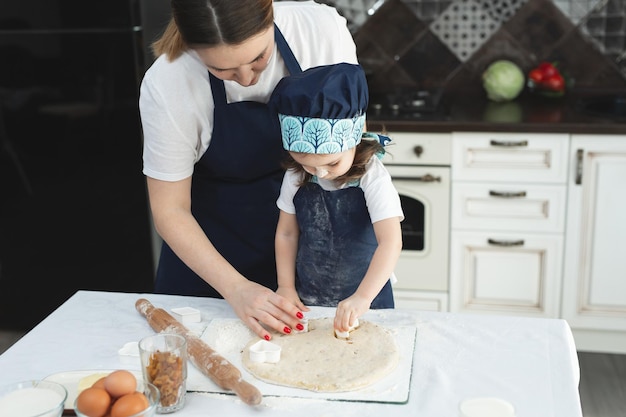 Mother and her little daughter preparing pastry in the kitchen Little girl using metallic