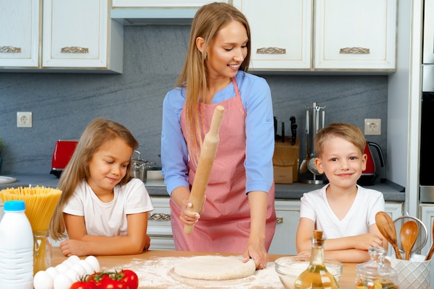 Mother and her little kids, boy and girl, helping her to prepare dough