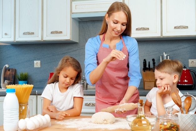 Mother and her little kids, boy and girl, helping her to prepare dough