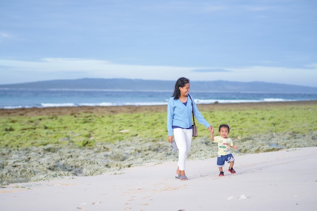 mother holding child's hand walking on the beach