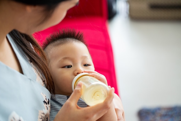 Mother holding to feed milk her baby at home.