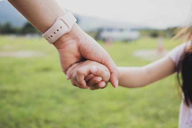 Mother holding hands with his daughter walking in a grass field green nature Love and care concept