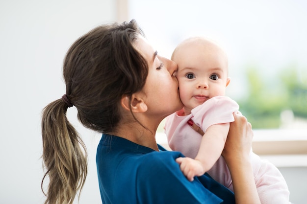 mother holding and kissing baby daughter at home