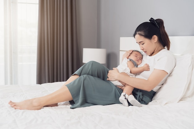 Mother holding newborn baby sleeping in her arm on a bed