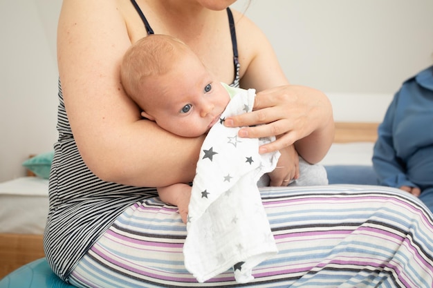 Mother holding and rocking baby sitting on fitball