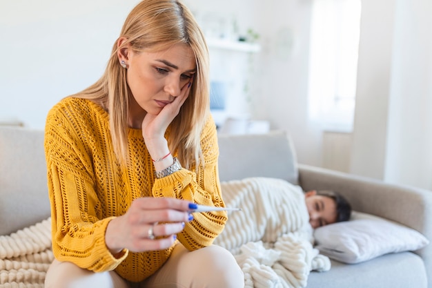 Mother at home and measure a temperature on her sick child. Sick little boy sitting on bed. The boy has a head ache and fever. The mother is comforting the boy.