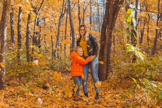 Mother hugging her child during walk in autumn park. Fall season and single parent concept.