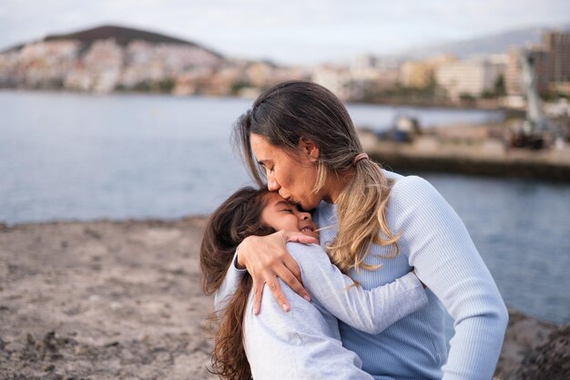 Mother hugging her little daughter on a walk by the sea and giving her daughter a lot of love Concept motherhood love growth