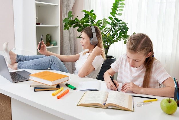 Mother is not helping daughter to do homework while using her smart phone and listening to music with headphones