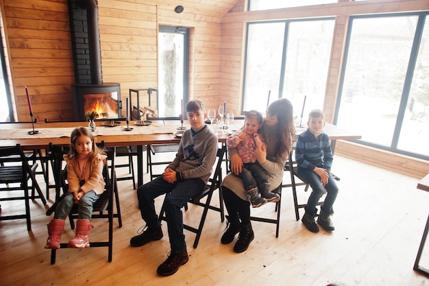 Mother and kids in modern wooden house sitting against table and fireplace spending time together in warm and love