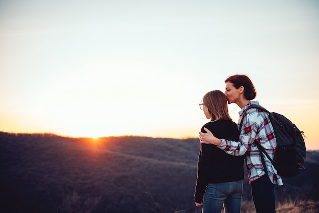 Mother kissing her daughter on a mountain at sunset