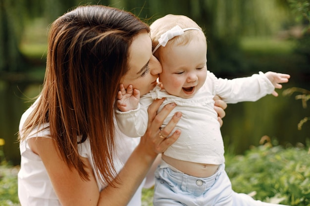 Mother and little baby daughter sitting in the park and posing for a photo. Family wearing white and light blue clothes