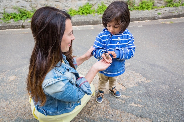 Mother and little eastern handsome baby boy playing outdoor with a snail