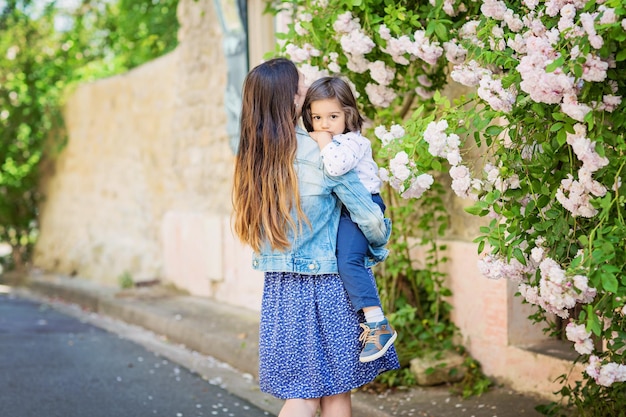 Mother and little handsome baby boy looking at bush with white roses