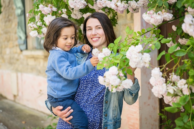 Mother and little handsome baby boy looking at bush with white roses