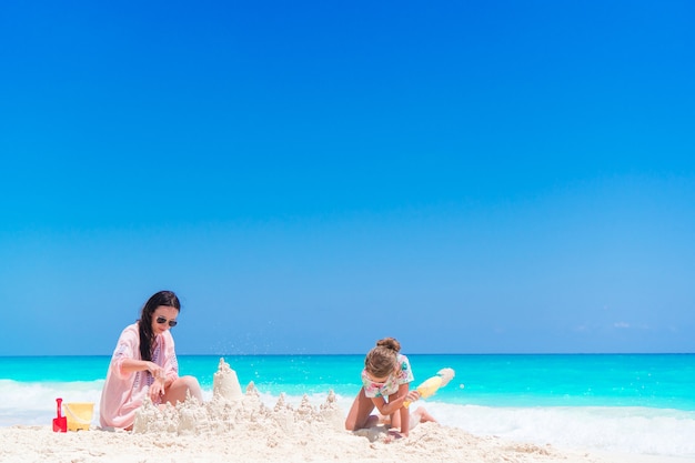 Mother and little kid making sand castle at tropical beach