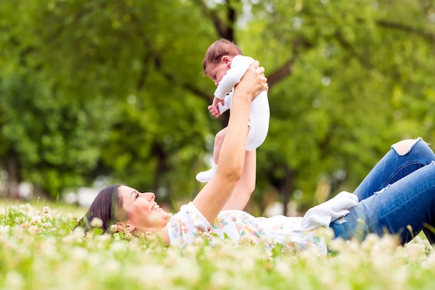 A mother lying on the grass while holding her baby