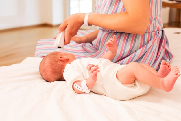 Mother measures newborn baby temperature on the bed