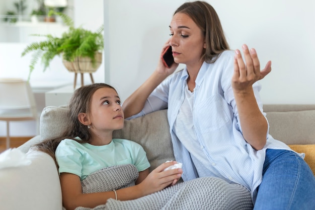 Mother measuring temperature of her ill kid. Sick child with high fever laying in bed and mother holding thermometer. Mother with cell phone calling to doctor