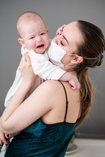 Mother in medical protective mask holds her baby in her arms during the coronovirus pandemic and covid-19