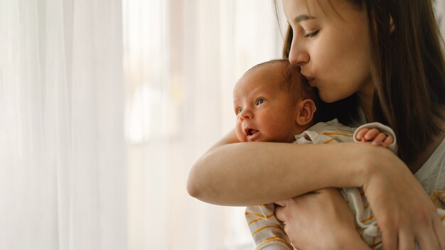 Mother playing with newborn baby son at home near the window