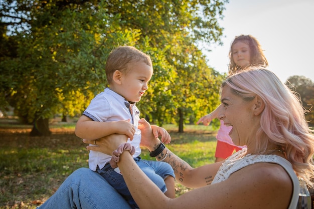 Mother plays with her son and makes him sit on her lap the daughter in the background mother relationship with her children