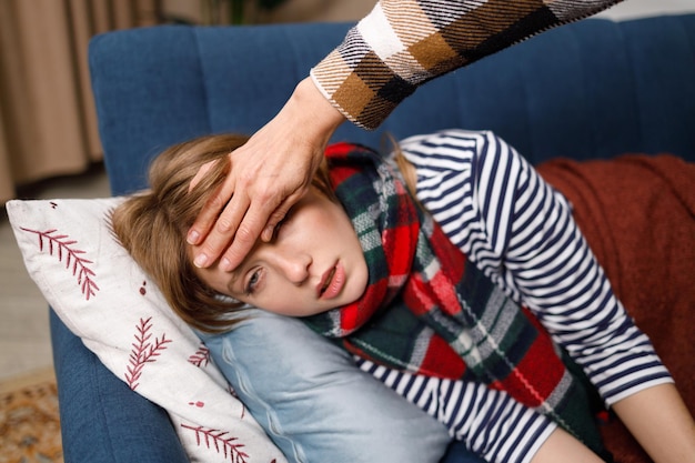 Mother put her hand on the forehead of her daughter who is sick with the flu