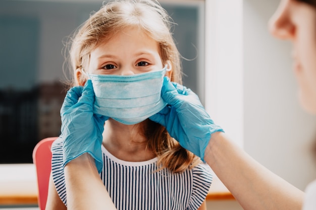 Mother puts on her baby sterile medical mask. Little girl and mom in medical mask. vaccination of children