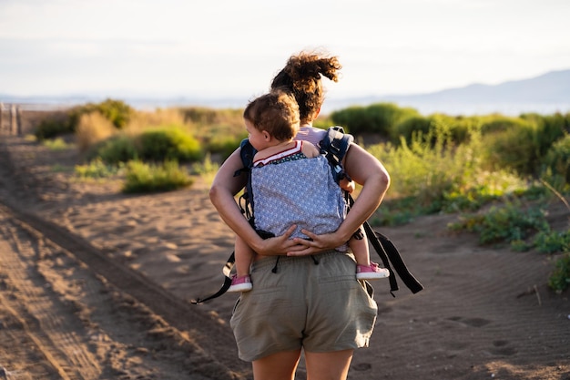 Mother running while carrying a baby on her back in a baby carrier outdoors