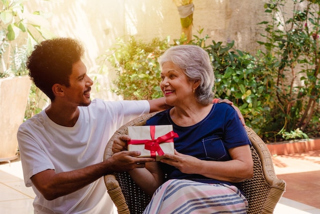 Mother's Day Caucasian mother and her black son with gift in the house garden Happy interracial family