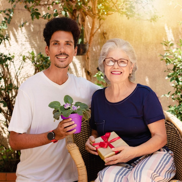 Mother's Day Caucasian mother and her black son with gift in the house garden Happy interracial family