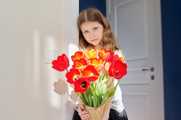 Mother's day girl child with bouquet of red tulips flowers at home