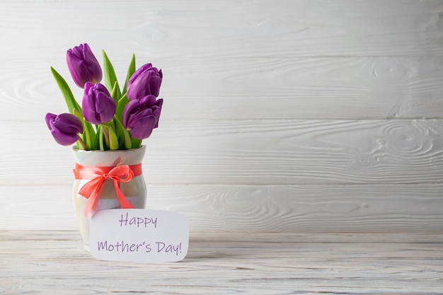 Mother's Day holiday card with a bouquet of fresh purple tulips in a vase with a pink bow