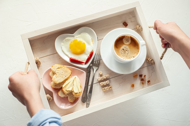 Mother's Day.  On the tray there is a cup of coffee, two plates of scrambled eggs and heart-shaped bread and the inscription I Love You Mom. View from above.