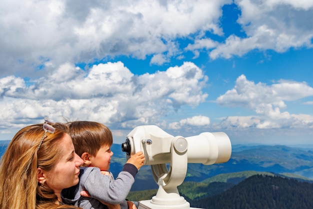 Mother shows son landscapes in valley of Rhodope Mountains and sky through telescope on observation tower of Snezhan