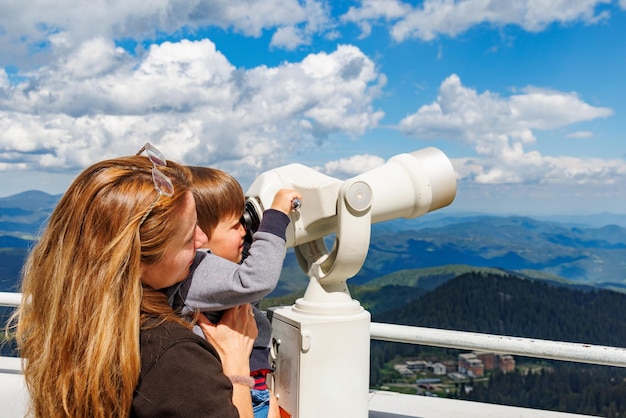 Mother shows son landscapes in valley of Rhodope Mountains and sky through telescope on observation tower of Snezhan