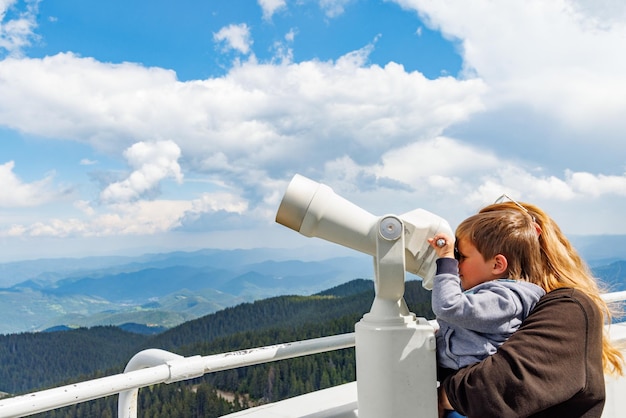 Mother shows son landscapes in valley of Rhodope Mountains and sky through telescope on observation tower of Snezhan